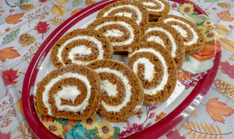Freshly sliced pumpkin rolls filled with creamy frosting, neatly arranged on a decorative platter with a festive fall-themed tablecloth at the Thanksgiving 2024 'Friendsgiving' Event by Home Not Alone Caregiver Services for individuals with intellectual disability (IDD) within residential group homes and accessible family group homes in Allegheny County, Pittsburgh, Pennsylvania.