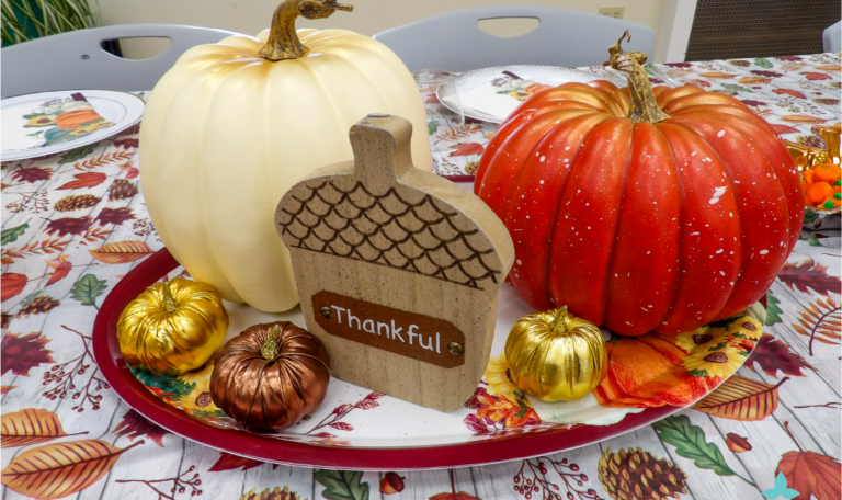 An elegant fall centerpiece featuring white and orange pumpkins, gold-painted mini pumpkins, and a 'Thankful' sign on a decorative tray at the Thanksgiving 2024 'Friendsgiving' Event by Home Not Alone Caregiver Services for individuals with intellectual disability (IDD) within residential group homes and accessible family group homes in Allegheny County, Pittsburgh, Pennsylvania.