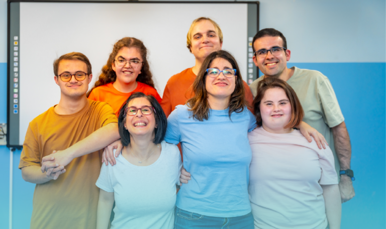 A group of seven individuals, including men and women with intellectual and developmental disabilities, smile together in a classroom. They stand closely, showing a sense of friendship and support. This image highlights inclusion during Developmental Disabilities Awareness Month (DDAM). Provided by Home Not Alone Caregiver Services for individuals with intellectual disability (IDD) within Community for Disabled Adults and accessible family group homes in Allegheny County, Pittsburgh, Pennsylvania.