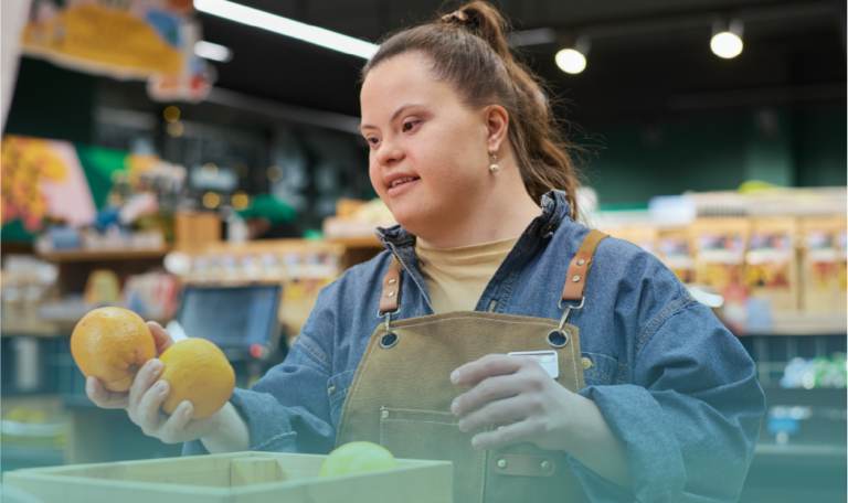 A young woman with Down syndrome works in a grocery store, wearing a denim jacket and a brown apron. She is sorting oranges with a focused expression. The background shows shelves stocked with various products. This image highlights workplace inclusion and independence for individuals with Down syndrome on World Down Syndrome Day. Provided by Home Not Alone Caregiver Services for individuals with intellectual disability (IDD) within Community for Disabled Adults and accessible family group homes in Allegheny County, Pittsburgh, Pennsylvania.