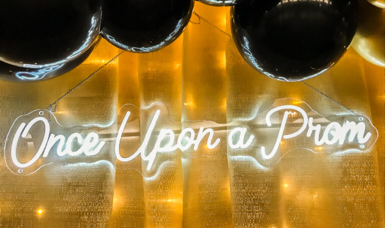 A glowing neon sign reading “Once Upon a Prom” displayed with golden drapery and black balloons as part of the prom decorations. Provided by Home Not Alone Caregiver Services for individuals with intellectual disability and Autism (ID/A) within Community for Disabled Adults and accessible family group homes in Allegheny County, Pittsburgh, Pennsylvania.