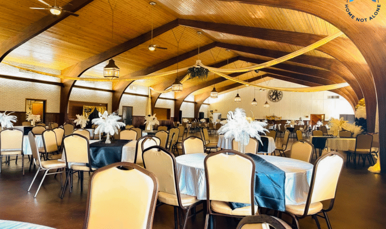 A wide view of the ballroom filled with decorated tables, black table runners, and white feather centerpieces prepared for the prom event. Provided by Home Not Alone Caregiver Services for individuals with intellectual disability and Autism (ID/A) within Community for Disabled Adults and accessible family group homes in Allegheny County, Pittsburgh, Pennsylvania.
