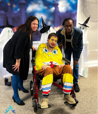A caregiver and an individual posing together and smiling during the Home Not Alone Halloween celebration, surrounded by festive decorations. Provided by Home Not Alone Caregiver Services for individuals with intellectual disability and Autism (ID/A) within Community for Disabled Adults and accessible family group homes in Allegheny County, Pittsburgh, Pennsylvania.