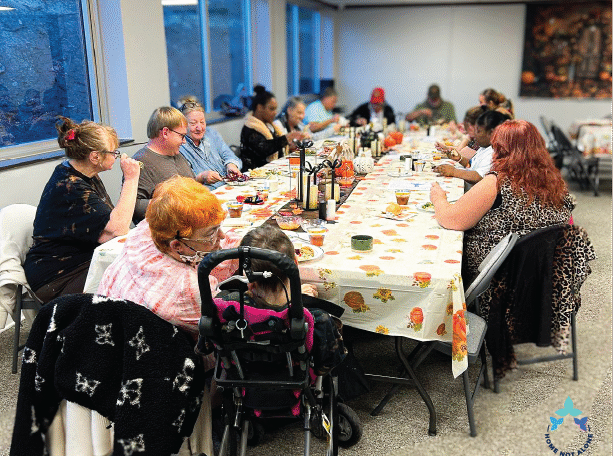 Attendees sitting together and enjoying warm conversation around the Thanksgiving table during the Home Not Alone Friendsgiving event. Provided by Home Not Alone Caregiver Services for individuals with intellectual disability and Autism (ID/A) within Community for Disabled Adults and accessible family group homes in Allegheny County, Pittsburgh, Pennsylvania.