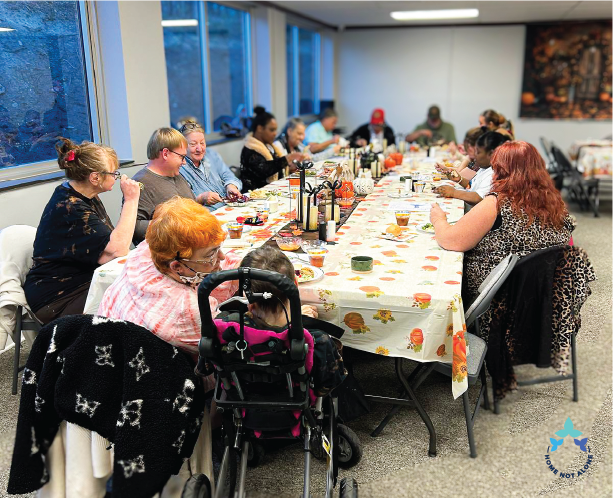 Attendees sitting together and enjoying warm conversation around the Thanksgiving table during the Home Not Alone Friendsgiving event. Provided by Home Not Alone Caregiver Services for individuals with intellectual disability and Autism (ID/A) within Community for Disabled Adults and accessible family group homes in Allegheny County, Pittsburgh, Pennsylvania.
