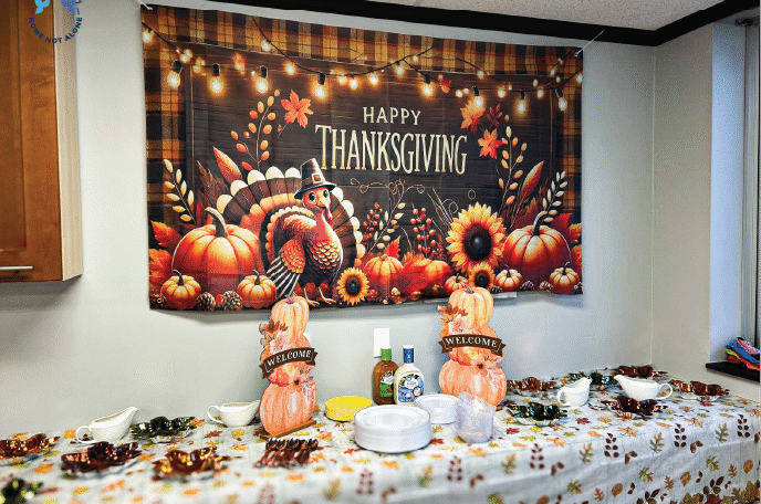 A festive Thanksgiving display featuring a large “Happy Thanksgiving” banner with pumpkins and a turkey, set above a decorated table during the Home Not Alone Friendsgiving event. Provided by Home Not Alone Caregiver Services for individuals with intellectual disability and Autism (ID/A) within Community for Disabled Adults and accessible family group homes in Allegheny County, Pittsburgh, Pennsylvania.
