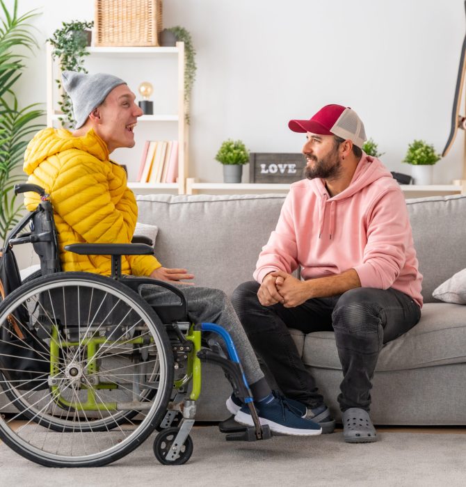 Disabled man in wheelchair and friends chatting relaxed in the living room of the house